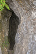 © HB - Atmospheric entrance to a dark, mysterious cave, framed by textured rock and hints of greenery.