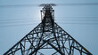 © jatupron - A towering electricity pylon against a clear blue sky, showcasing the structure's intricate metal framework and overhead power lines.