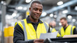 © Maksym - Moment of quiet focus as a Black warehouse worker checks labels on a delivery cart, reflective vest glowing under overhead lamps, colleagues moving carts blurred in background to c
