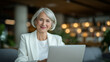 © Maksym - Attractive aged woman in smart attire navigating a laptop with ease, surrounded by soft lighting, modern shelving, and subtle interior textures that convey a calm, productive setti