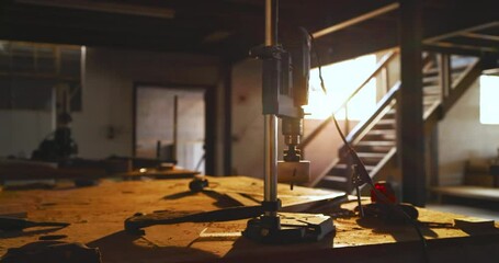 Camera is panning across sunlit dusty workbench as drill press is entering frame for feature reveal