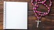 © Putra - A blank spiral-bound notebook and a pink rosary on a wooden surface.