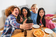 © Koldo_Studio - Four cheerful young multi ethnic friends are taking a selfie with a smartphone while enjoying pizza and drinks at home