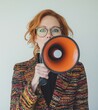 © Lotus Frames - Confident redhead professional, donning glasses and a vibrant coat, commands attention with a megaphone in hand, her expression resolute.