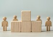 © Noppakun - Wooden blocks stacked in a podium style with wooden human figures standing behind, symbolizing leadership and teamwork.