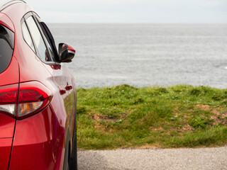 Wall Mural - A red car is parked on the side of a road overlooking the ocean. Travel and tourism. Trip to nature, cloudy day, rough stone coast. Sightseeing landmarks. West of Ireland.