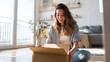 © Alex - A happy young woman sits on her living room floor, smiling as she opens a long-awaited delivery.