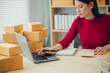 © ThawKyar - Asian female small business owner working from home taking orders and shipping to customers with laptop, pen and notepad. Ecommerce concept for SMEs.