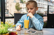 © Elena - Child Drinking Orange Juice While Sitting at a Table