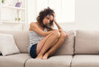 © Prostock-studio - Young lonely african-american woman sitting on couch at home. Thoughtful, sad girl hiding from the world, copy space. Depression, stress concept