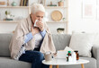 © Prostock-studio - Coronavirus Symptoms. Sick Senior Woman Coughing Hard At Home, Sitting On Couch Covered With Blanket, Free Space
