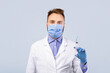 © Prostock-studio - Immunization concept. Young male doctor wearing protection, holding syringe with coronavirus vaccine over grey studio background. Medical worker with innovative drug for intramuscular injection