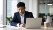 © photostockatinat - A Focused Asian Businessperson Working on a Laptop in the Office