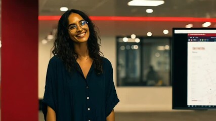 Woman with glasses smiles in an office Red walls and screen display data (AI Video)