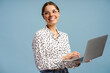 © Maria Vitkovska - Smiling businesswoman using laptop and looking away on blue background