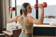 © Maria Vitkovska - Athletic woman lifting dumbbells and listening to music with headphones during home workout