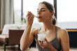 © Maria Vitkovska - Young attractive woman eating yogurt after fitness training at home