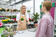 © sofiko14 - A florist helps a customer pay for a purchase at the checkout, with a smile, holding a small plant in a pot.