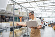 © sofiko14 - A man in a shop with a laptop looks at the flowerpots on the shelves, browsing and making a choice.