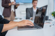 © panomporn - Group of business partners gathered around open laptop discussing company development strategies in modern office.