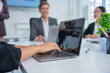 © panomporn - Group of business partners gathered around open laptop discussing company development strategies in modern office.