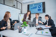 © panomporn - Group of business partners gathered around open laptop discussing company development strategies in modern office.