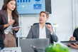© panomporn - Group of business partners gathered around open laptop discussing company development strategies in modern office.