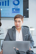 © panomporn - Group of business partners gathered around open laptop discussing company development strategies in modern office.