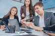 © panomporn - Group of business partners gathered around open laptop discussing company development strategies in modern office.