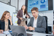 © panomporn - Group of business partners gathered around open laptop discussing company development strategies in modern office.