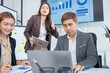 © panomporn - Group of business partners gathered around open laptop discussing company development strategies in modern office.