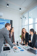 © panomporn - Group of confident professional business people pointing at graphs and charts to analyze marketing data to plan new sales strategies to increase productivity in modern office.