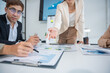 © panomporn - Group of confident professional business people pointing at graphs and charts to analyze marketing data to plan new sales strategies to increase productivity in modern office.