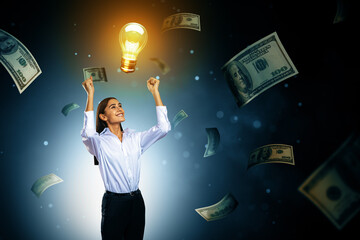 Wall Mural - successful businesswoman celebrating idea with glowing lightbulb and floating money on dark backgrou