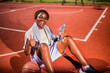 © djoronimo - Young black woman practicing basketball alone at sports court in the morning. She is holding bottle of water and showing thumbs up.