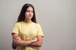 © Lomb - Confident teenage girl in yellow t-shirt with crossed arms standing against blank neutral background