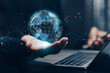 © teerawat - Global network and digital connection: A businessman's hand holds a glowing holographic globe above a laptop, surrounded by abstract digital waves and data points representing worldwide communication.