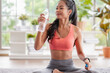 © weedezign - Young asian woman take a rest after training and drinking water  after workout in living room