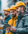 © Thanakorn - Engineers in hard hats collaborating on construction project, focused on tablet. Their teamwork and concentration highlight importance of safety and planning