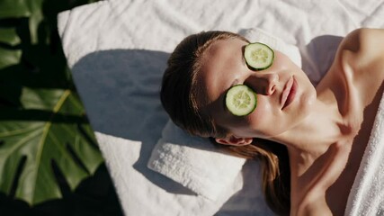 Poster - Wellness spa treatment featuring young woman relaxing on massage bed, wearing cucumber slices over eyes during soothing skincare rejuvenation process