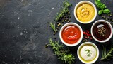 Four bowls of various sauces and dressings on a dark stone surface with fresh herbs and spices.