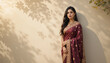 © DhanShalik - Elegant Woman in Maroon Sari: A captivating portrait of a young woman, exuding grace and elegance, standing against a textured wall adorned with leaf shadows. She is draped in a rich maroon sari.