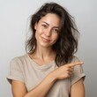 © vilaiporn - An attractive woman smiling and pointing, exuding confidence and positivity in a neutral background.