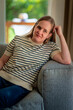 © sepy - A visually impaired woman with blonde hair sitting on a sofa in her cozy home. Smiling female wearing casual clothes.