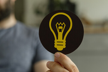 Aufkleber - A hand holds a circular card with a lightbulb symbol, representing ideas and innovation.