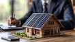 © Jack - Homme d'affaire faisant un étude de rentabilité des panneaux solaire photovoltaïque, maquette de maison sur bureau en bois