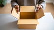 © Curioso.Photography - Person holding and opening an empty cardboard box on a white table.