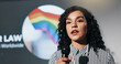 © peopleimages.com - Microphone, presentation and stage with woman in auditorium for speech on worldwide lgbt laws. Awareness, community or gender equality and speaker on podium with rainbow flag for gay rights or pride