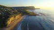 © Thanthara - Aerial view of serene beach with cliffs, golden light, and calm waters