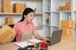 © wichayada - Small Business Logistics. Young woman managing packages and online tasks.